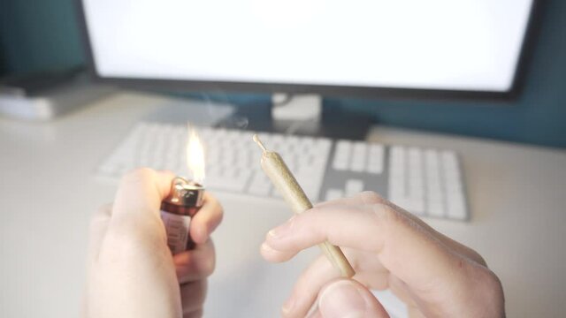 Smoking Weed at Computer Station. Close-up of a Hand Holding a Legal Cannabis Joint.