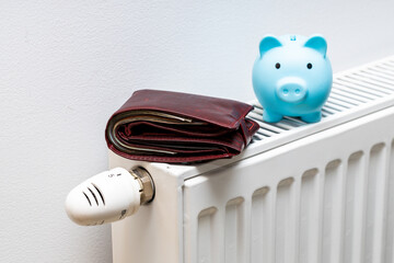 A stuffed wallet lying on the radiator and a small blue piggy bank, The concept of rising apartment...
