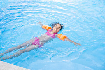 Fototapeta na wymiar Pretty little girl swimming in outdoor pool and have a fun