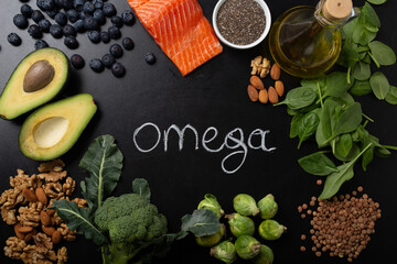 Healthy food with good fat sources, ingredients rich in Omega−3 fatty acids: salmon, vegetables, berries, nuts, seeds, olive oil, black chalk board top view, hand chalk written "omega" in center 
