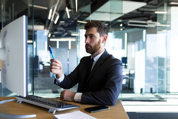 Serious and thoughtful male entrepreneur working in the office at the computer in a business suit