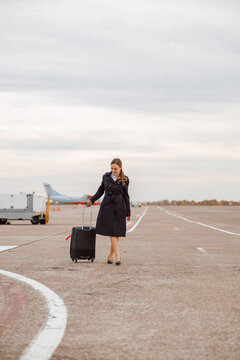 Cheerful woman with travel suitcase standing outdoors at airfield