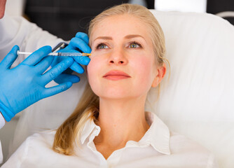 Closeup portrait of adult woman getting filler injections for facial skin tightening at aesthetic cosmetology clinic