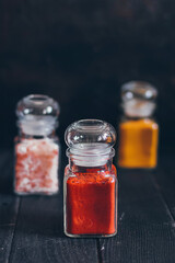 Bright aromatic spices in glass jars, assortments of spices: pink salt, paprika and turmeric on black stone background.