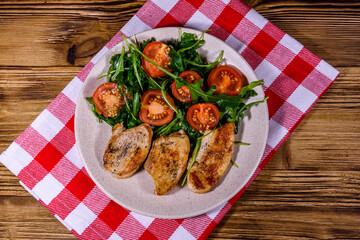 Roasted chicken breasts and salad with arugula and cherry tomatoes in a ceramic plate. Top view