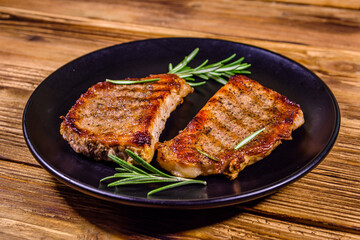 Plate with roasted steaks and rosemary twigs on a wooden table