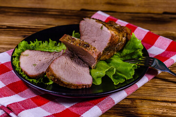 Slices of baked pork meat and lettuce leaves on a black plate