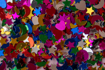 Pink, violet, yellow, green, blue, red stars, hearts, and moons confetti and glitter in macro. Abstract festive background. Light trendy silver shimmering parts for bright presentation color 2022