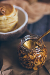 A glass jar of honey with nuts on wooden background