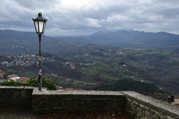 A street lamp on a stone wall against the backdrop of a mountainous landscape and houses on a...