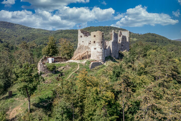 Fototapeta na wymiar Aerial view of under restoration medieval Reviste castle above the Hron (Garam) river in Slovakia with donjon, circular gate tower, ruined gothic palace blue cloudy sky 