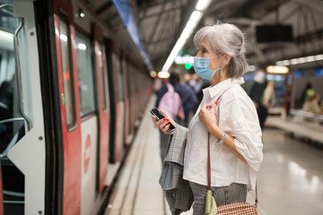 Elderly Caucasian woman in mask standing in metro station beside arrived train.