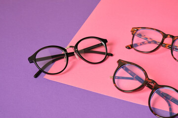 different eyeglasses on pink and purple geometric background, trendy eyeglass frames copy space - obrazy, fototapety, plakaty