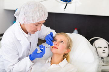 Naklejka premium Professional experienced female cosmetologist performing face contouring injections to adult woman in aesthetic medicine clinic