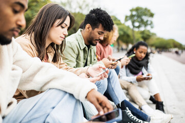 Group of young adult friends using smartphones outdoors - Addicted multiracial students chatting...