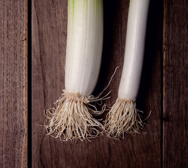 A leek on a rustic wooden table in a dark environment.