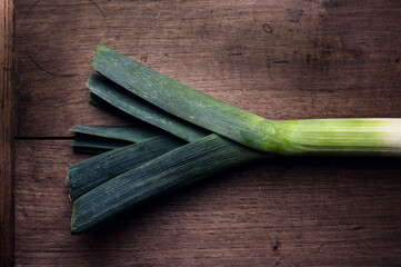 A leek on a rustic wooden table in a dark environment.