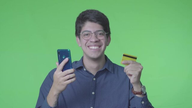 Hombre latino comprando en linea usando la tarjeta de cr&eacute;dito con fondo verde