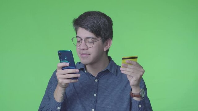 Hombre latino comprando en linea usando la tarjeta de cr&eacute;dito con fondo verde