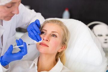 Closeup portrait of adult woman getting filler injections for facial skin tightening at aesthetic cosmetology clinic