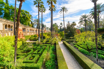 Naklejka premium The landscaped gardens of palm trees and manicured grounds inside the Royal Alcázar of Seville Spain.