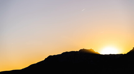 Ultimos rayos de sol entre la silueta de la montaña, avión cruzando el cielo
