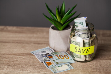 Dollar bills in glass jar and text save on wooden table