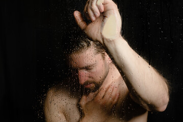 depressed man taking a shower perceives mental pain and starting to cry while lean on glass with hand