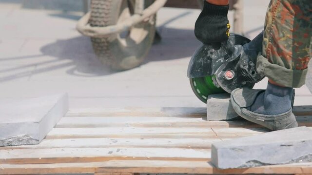 A worker cuts a granite slab with a grinder. Working process at a construction site. Work as a grinder at a construction site