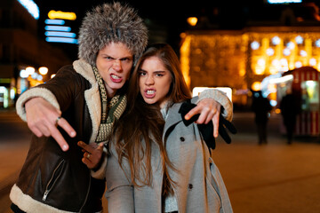 Male and female friends goofing off on the city streets , night out. showing some teeth and pointing with fingers  