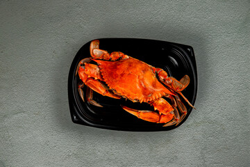 Cooked crab on black plastic plate on gray background.