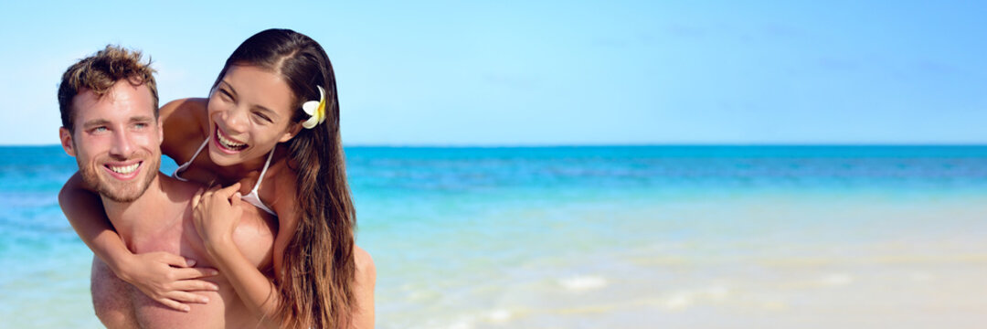 Happy beach couple laughing while piggybacking. Interracial relationship young man and woman walking on travel summer vacation having fun. - Powered by Adobe