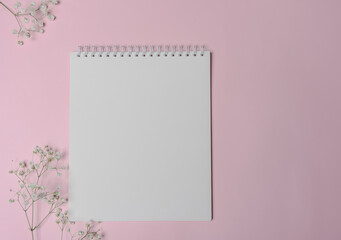  White spiral notebook with white smoll flowers. Copy space for the design. Blank square spiral notepad on pink background