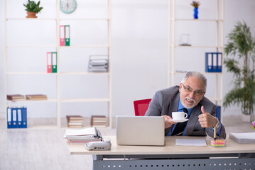 Old male employee drinking coffee during break