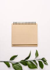 sketchbook brown sheet of paper notepad with spirals for planning top view and next to the leaf of green plant vertical view