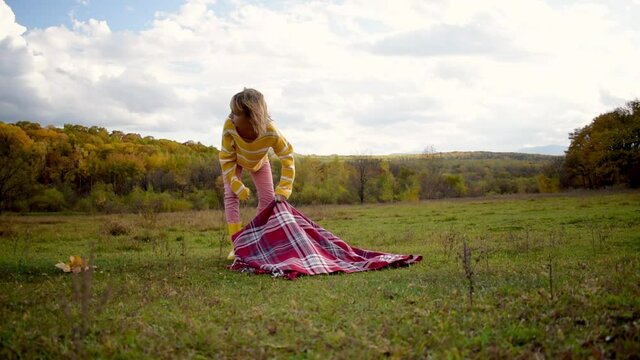 Child girl picks up a red blanket after a picnic in the meadow. People are one with nature. Wellness concept. Sense of balance and calmness.