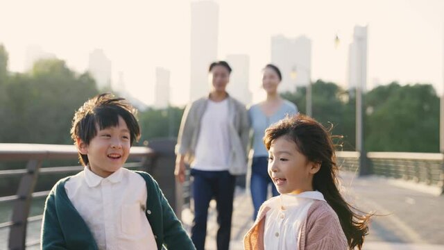 happy asian family with two children taking a walk in city park