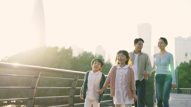 happy asian family with two children taking a walk in city park