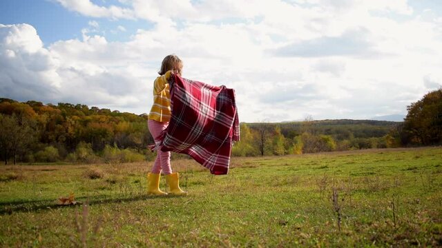 One girl holds a checkered plaid and walks slowly into the autumn forest. People are one with nature. Wellness concept. Health care, authenticity, a sense of balance and calmness.