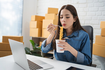 Asian businesswoman eating instant noodles after hard work. She is blowing noodles.
