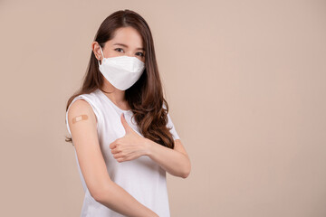 Young beautiful asian woman wearing mask and getting a vaccine protection the coronavirus. She showing thumbs up in studio background