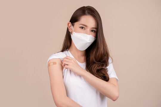 Asian woman in white mask showing plaster on shoulder after coronavirus vaccine on background, copy space. Vaccination, immunization, flu prevention concept. Getting Covid-19 vaccine