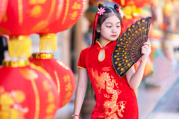 little Asian girl wearing red traditional Chinese cheongsam and holding a Fanningand lanterns with...