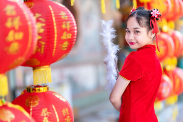 little Asian girl wearing red traditional Chinese cheongsam and holding a Fanningand lanterns with...