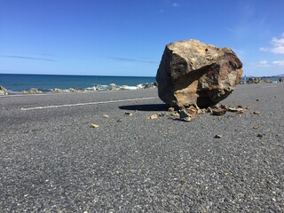 Rock dislodged by an earthquake sitting in the middle of a coastal road  