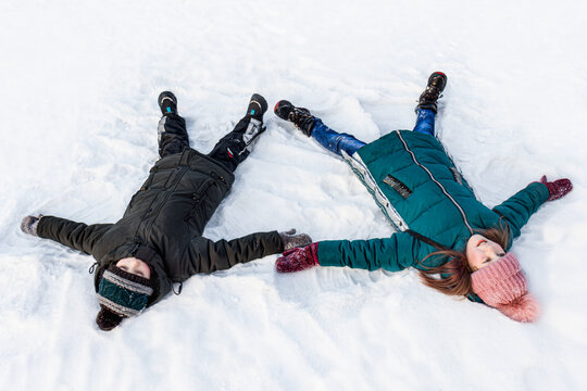 children brother and sister lie in the snow and make snow angels. Selective focus. Winter fun and snow games
