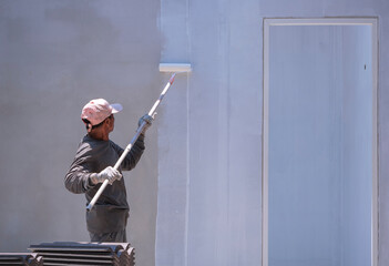 Asian builder worker using long handle roller brush to painting primer white color on concrete wall...
