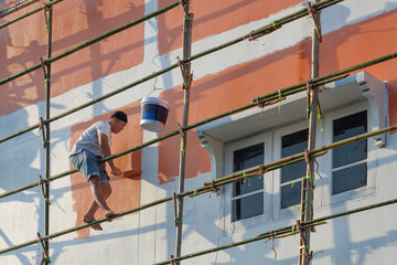 Low angle view of Asian painter on wooden scaffold is painting wall outside of the old house...