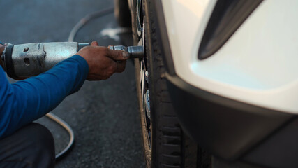 mechanic man using electric drill to loosen the bolts of vehicle wheel for changing a car tire