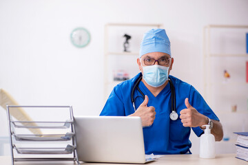 Old male doctor working in the clinic during pandemic